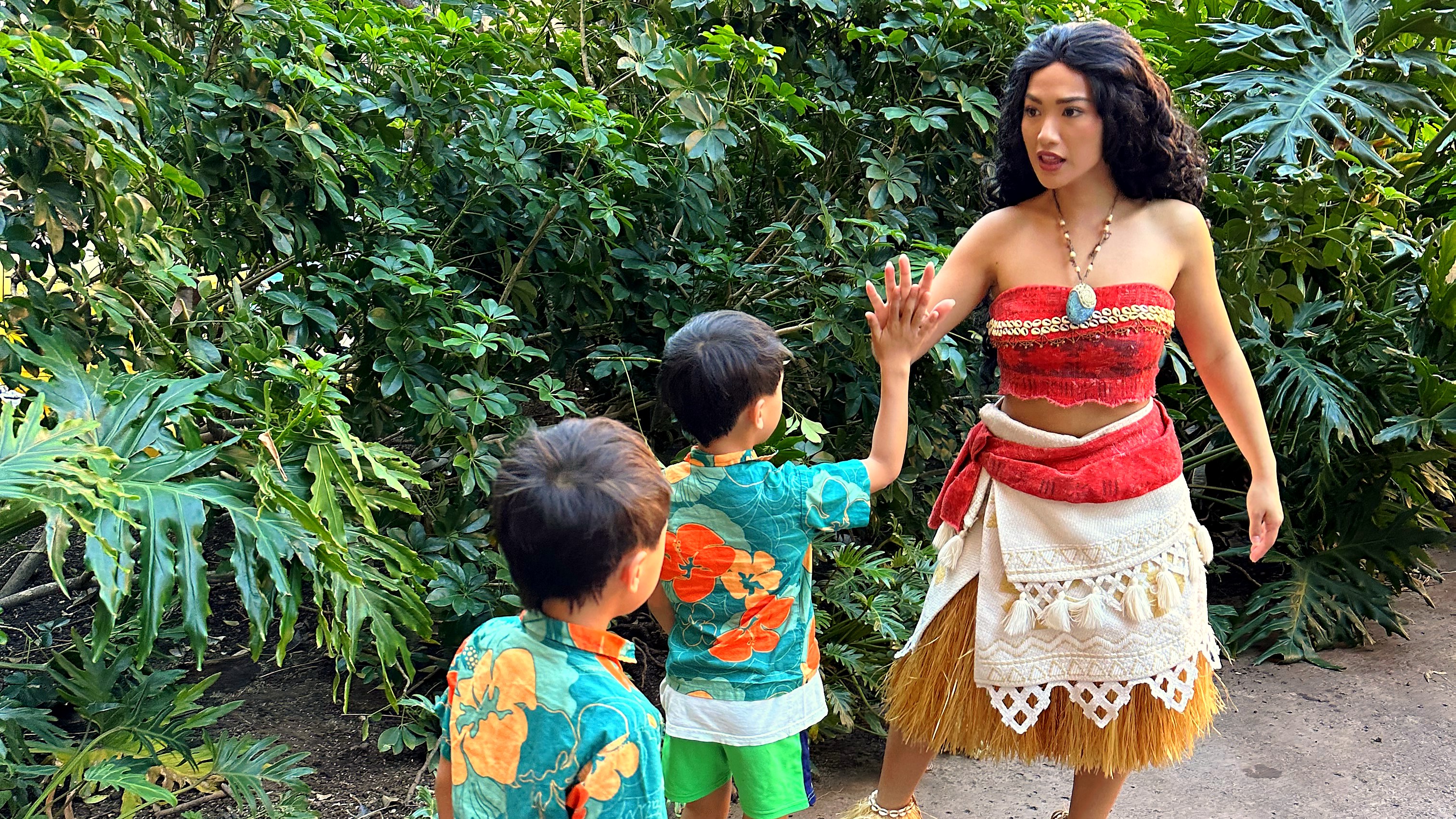 Two children meeting Moana at a Disney resort, surrounded by lush tropical foliage